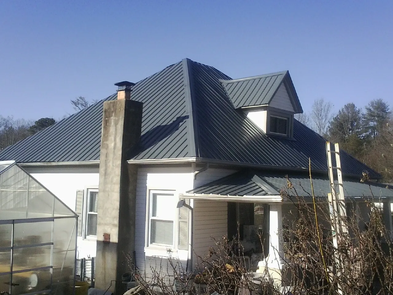 Dark blue standing seam metal roof on a white farmhouse with dormer — Slate & Tile Roof Repair by Roofing Brothers in Iva