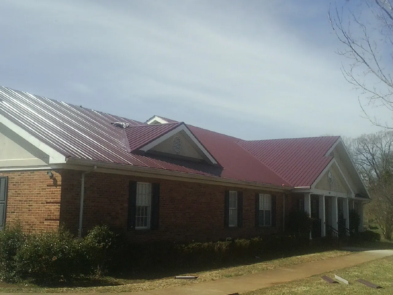 Red metal roof with gabled entries on a long brick building, from a Hail Damage Roof Repair job in Iva