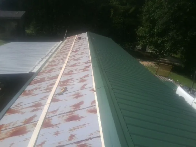 Old rusted panels beside newly installed green metal roofing — Wind Damage Roof Repair by Roofing Brothers in Iva