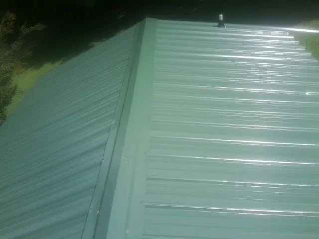 New green metal panels meeting at the ridge of a roof — Flat Roof Repair work by our crew in Iva