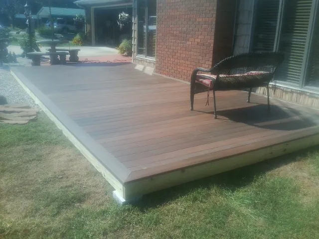 New wood deck and wicker chair beside a brick house in Iva