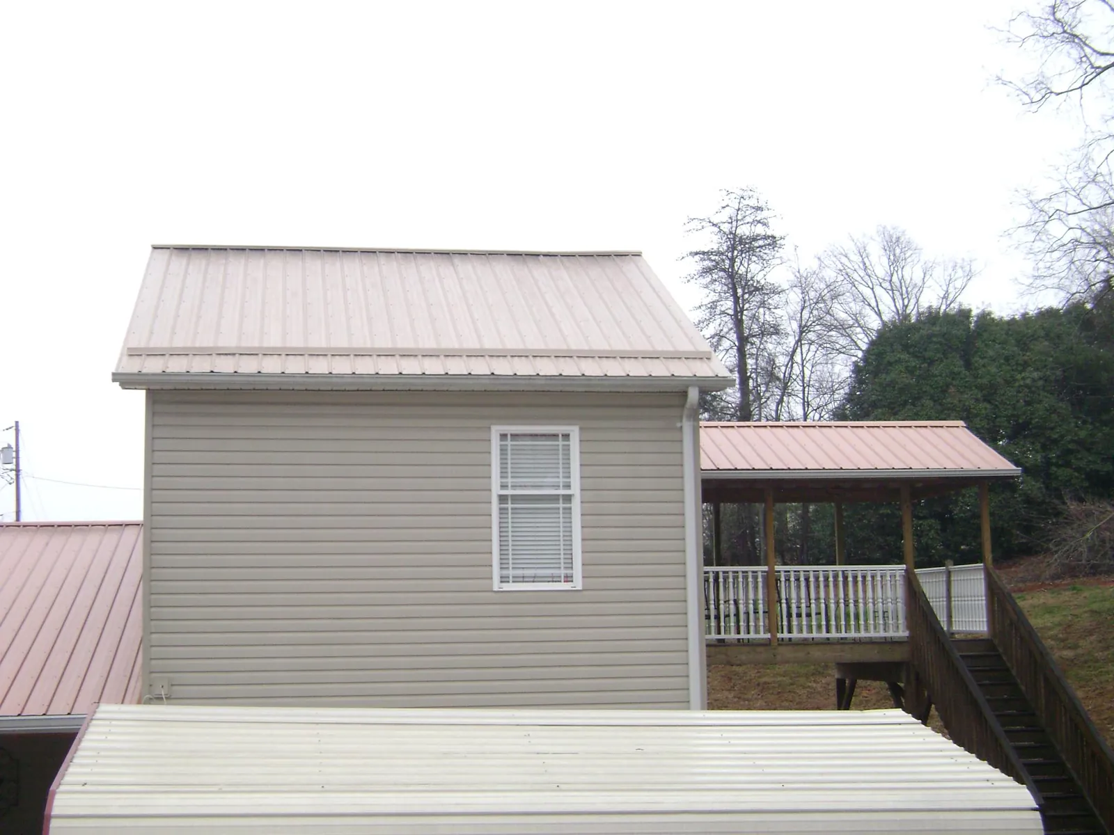Tan metal roofs on a two story addition and attached porch, from a Roof Replacement job in Iva